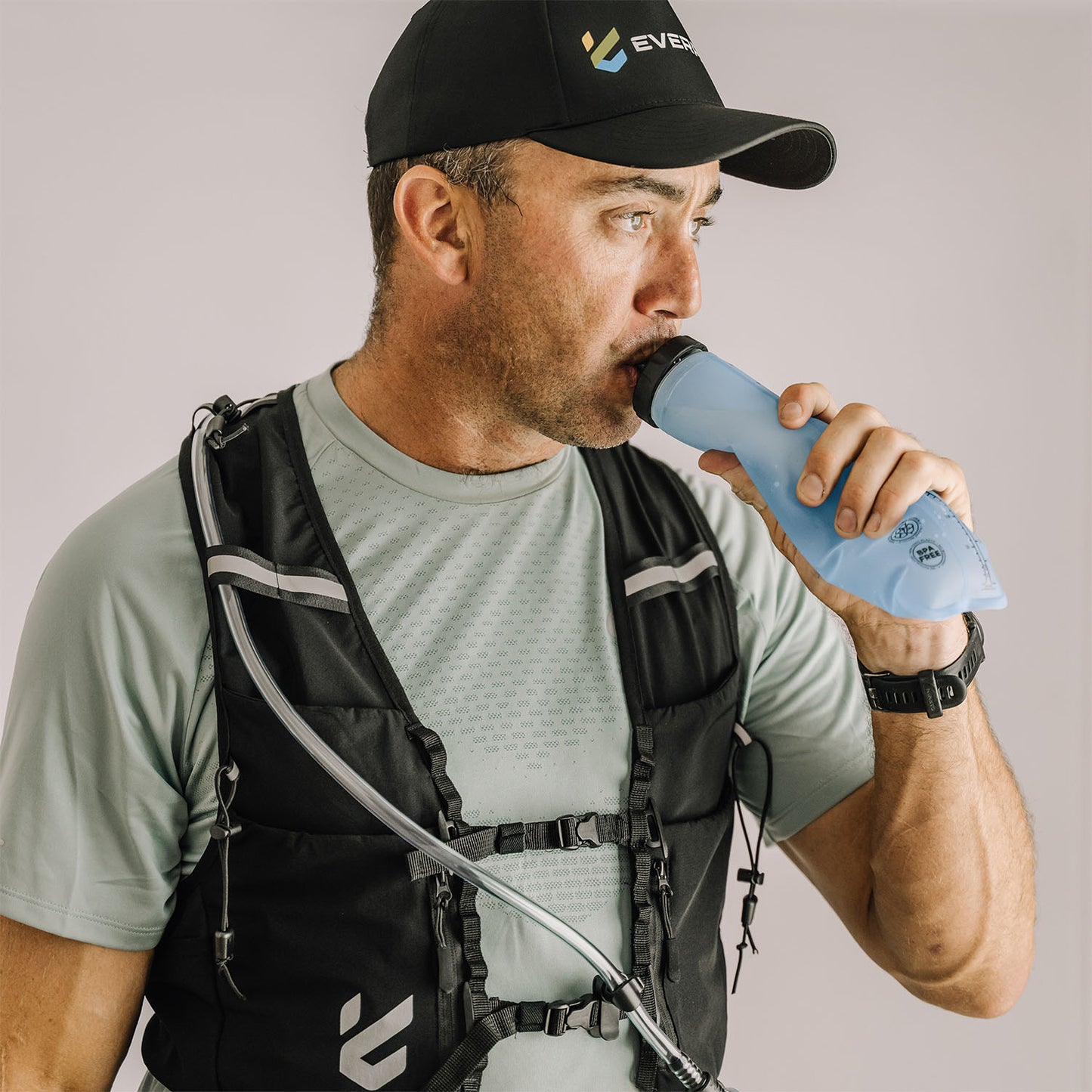 Man drinking from a water flask while wearing an Everpace running vest and cap with Everpace logo.