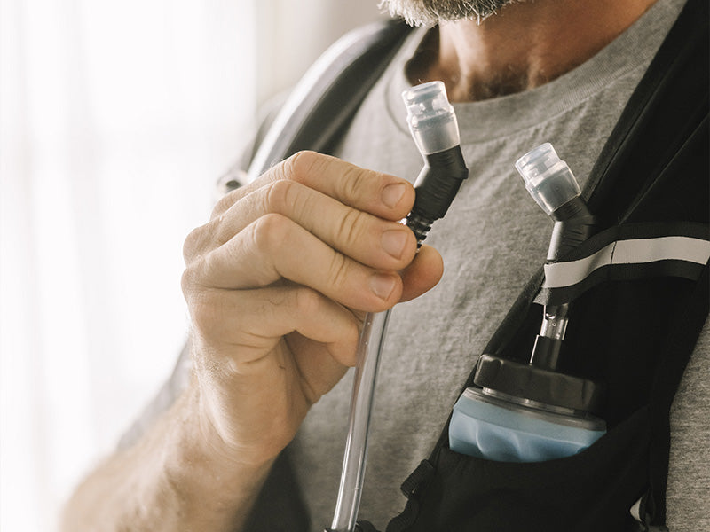 Person holding a bladder tube with a clear mouthpiece, wearing an Everpace vest and wearing a gray shirt.