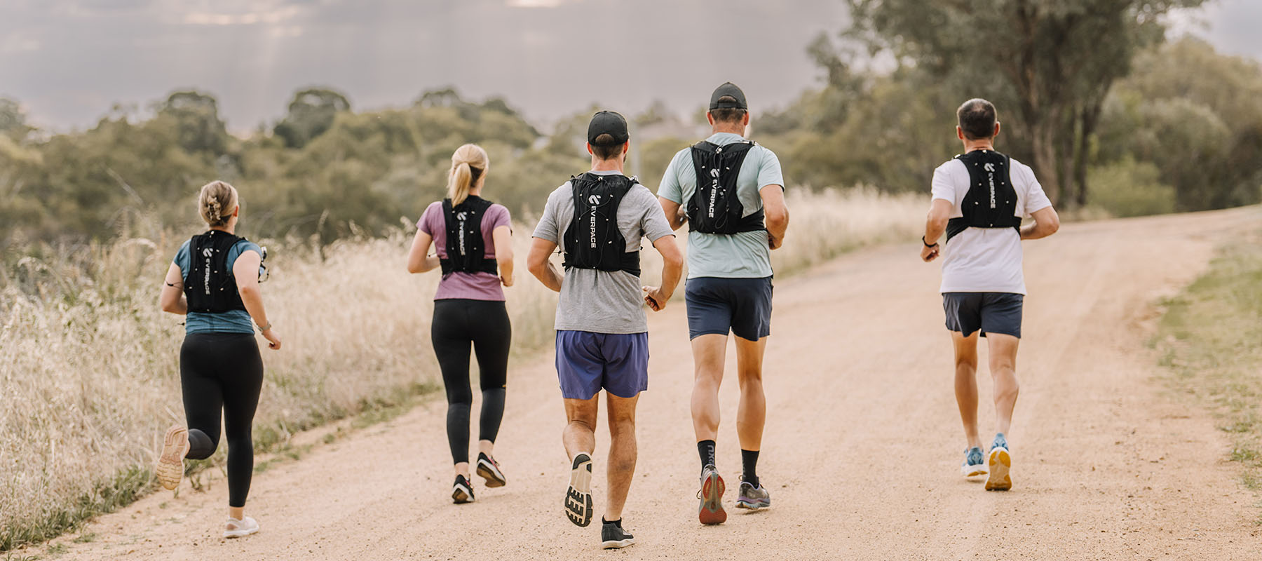 Five people running on a dirt trail, wearing Everpace running vests