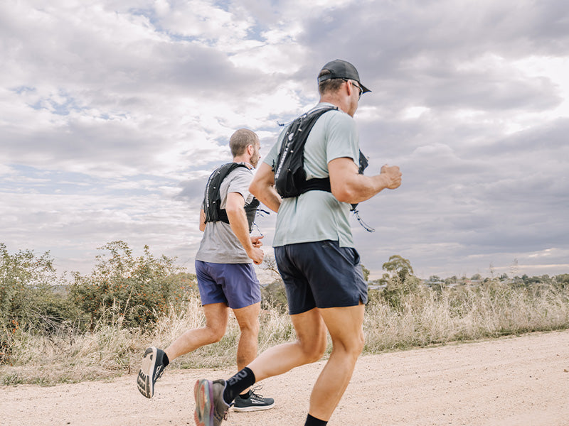 Two runners on a trail with Everpace vests against a cloudy sky